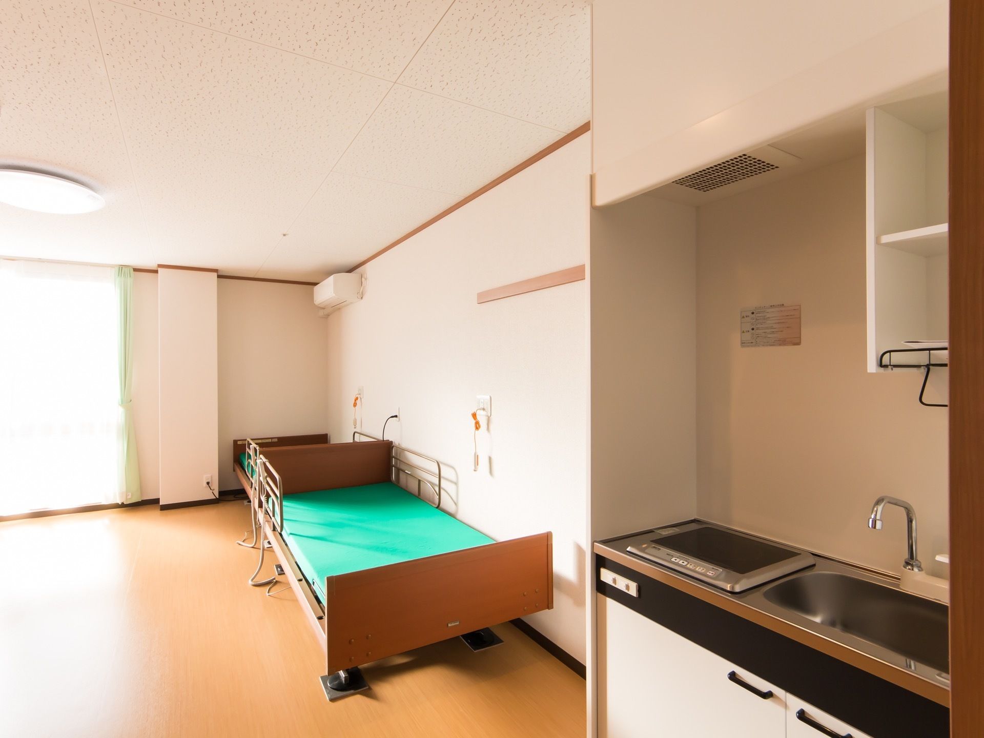 居室に洗面台が設置されている。IH調理器が一口あり、その上の天井に網目のカバーがついた換気扇が取り付けられている。