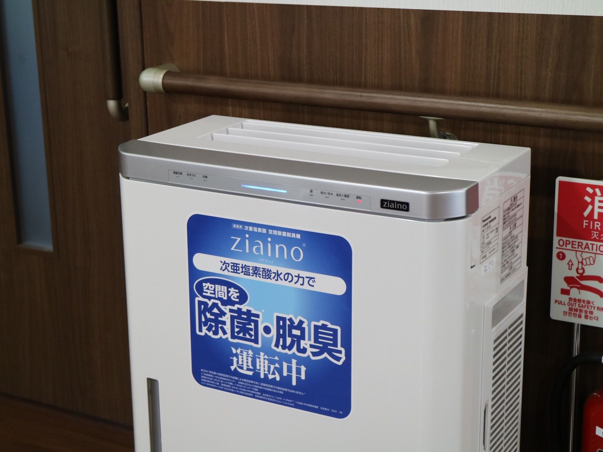 フロアの壁際に、空気清浄脱臭機が置かれている。横には消火器があり、壁には手すりがある。