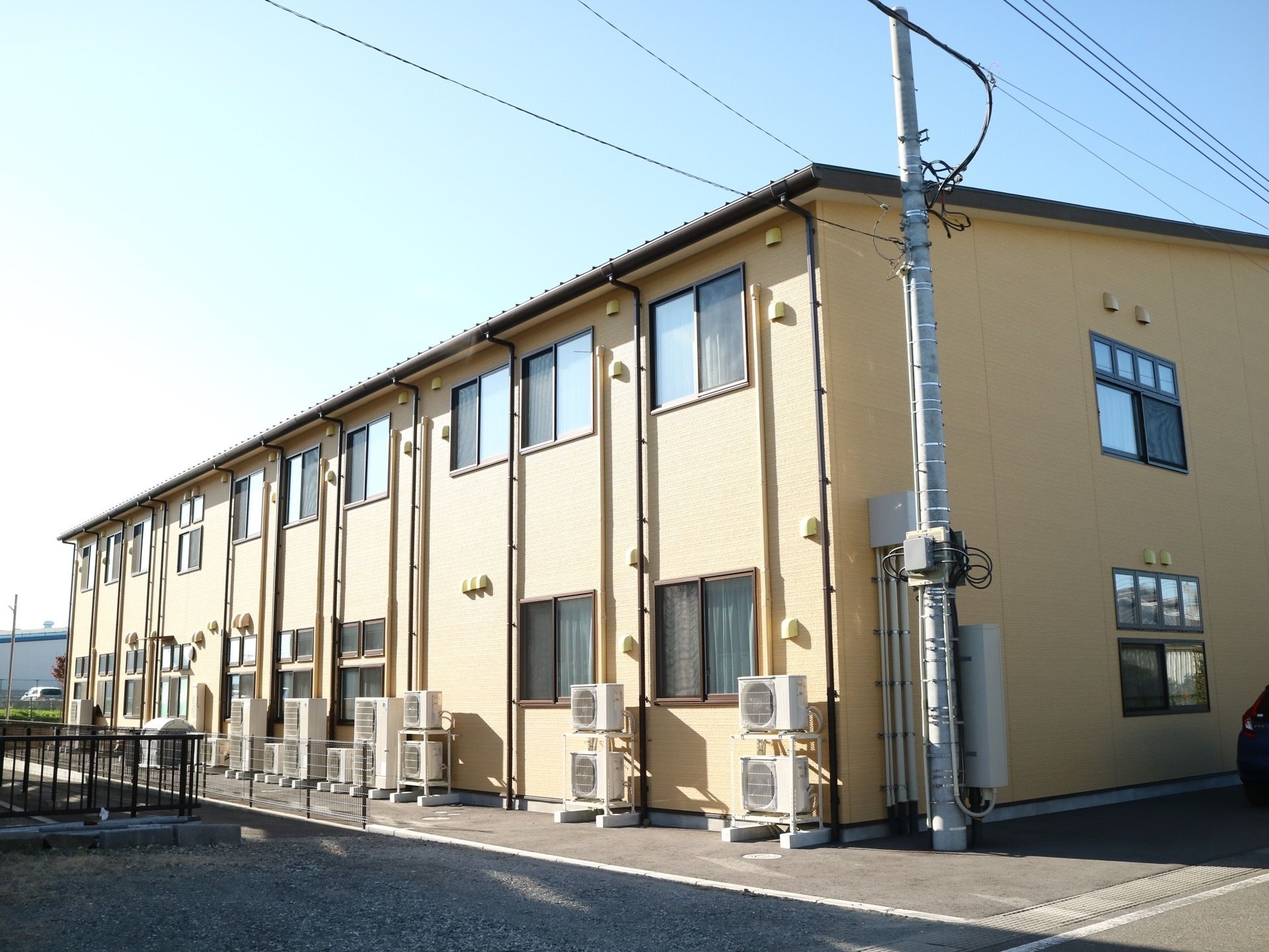 舗装された敷地に、クリーム色の外壁をした２階建ての住宅がある。窓が設置された面に、日差しが良く当たっている。