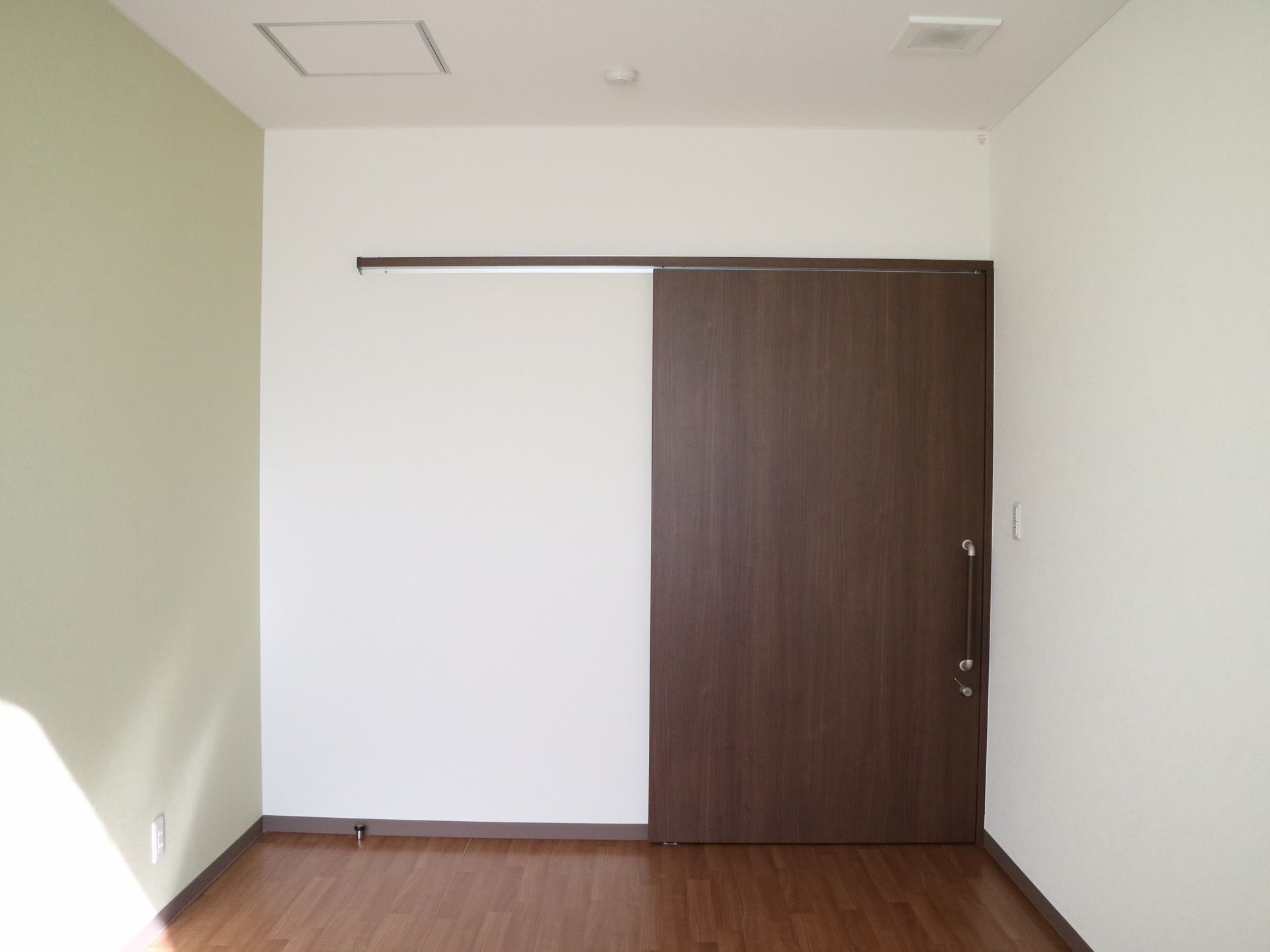 白い壁にフローリングの居室があり、部屋の中ほどまで陽が入っている。入り口は木目調の大きな引き戸になっている。