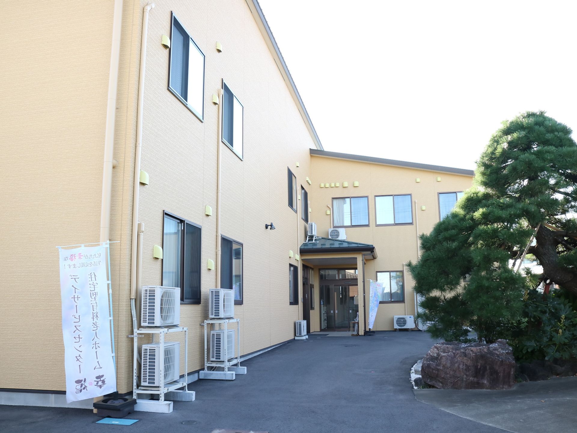 正面に松が植えられ、当館ののぼり旗がある2階建ての建物