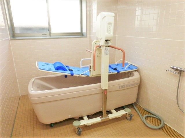 ブルーのシートが敷かれた機械浴が設置された浴室はタイル張りで窓もついている。