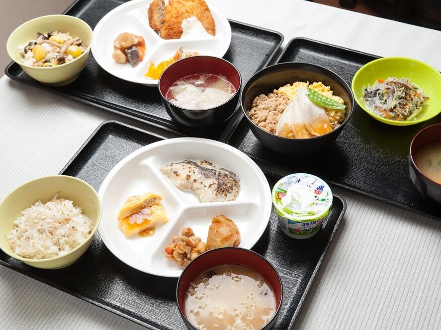 黒いトレーが３つあり、それぞれに丼物や肉料理をメインにした食事などが並び、汁物が添えられている。