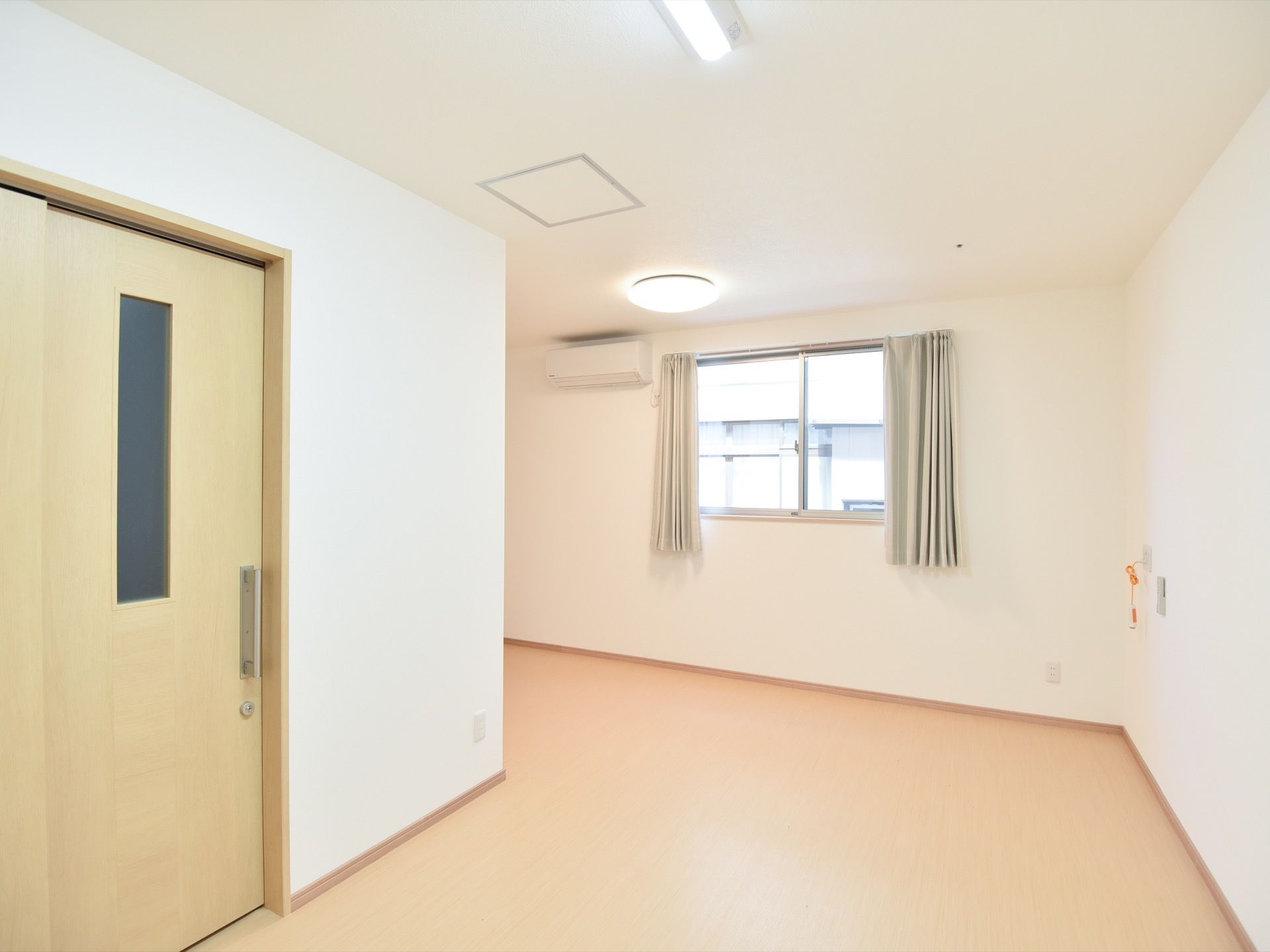 窓から日が入り、居室は明るく落ち着いた雰囲気。壁にはオレンジの紐が特徴的なナースコールが設置されている。