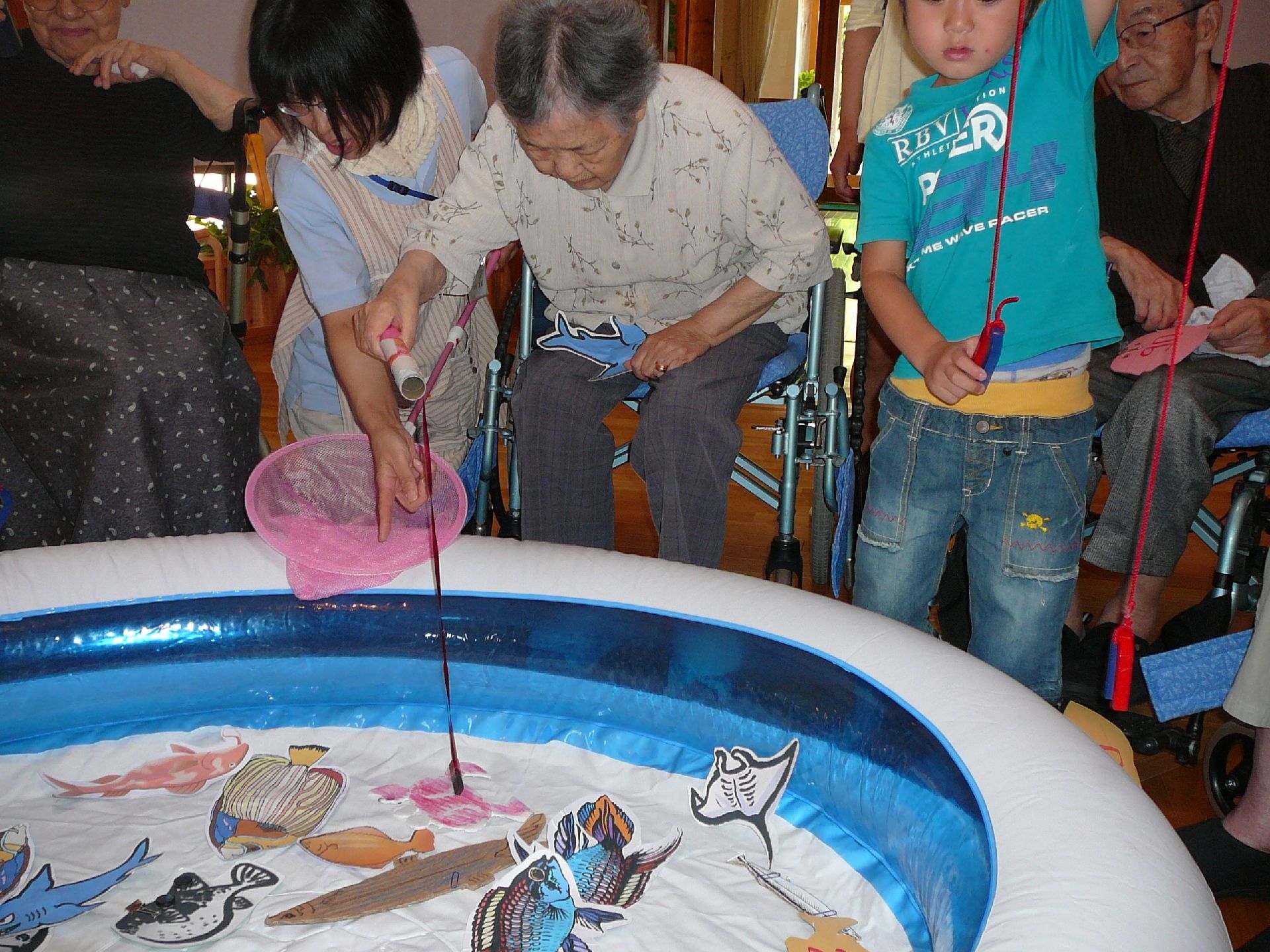 小さな子供と絵に書いた魚釣りを楽しむご入居者様とお手伝いする職員