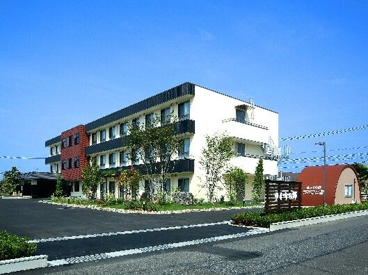 白を基調とした3階建ての建物の中央部分はブラウンで、玄関には車寄せが付いている。広い駐車場もある。
