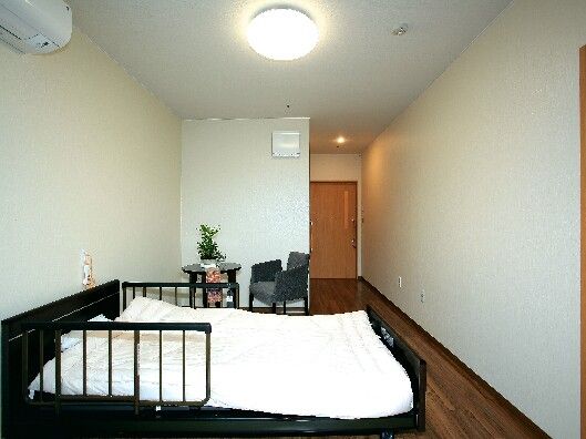 テーブルセットや寝具付きのベッド、大きな窓が付いたフローリングの部屋にはエアコンも完備され、観葉植物が飾られている。