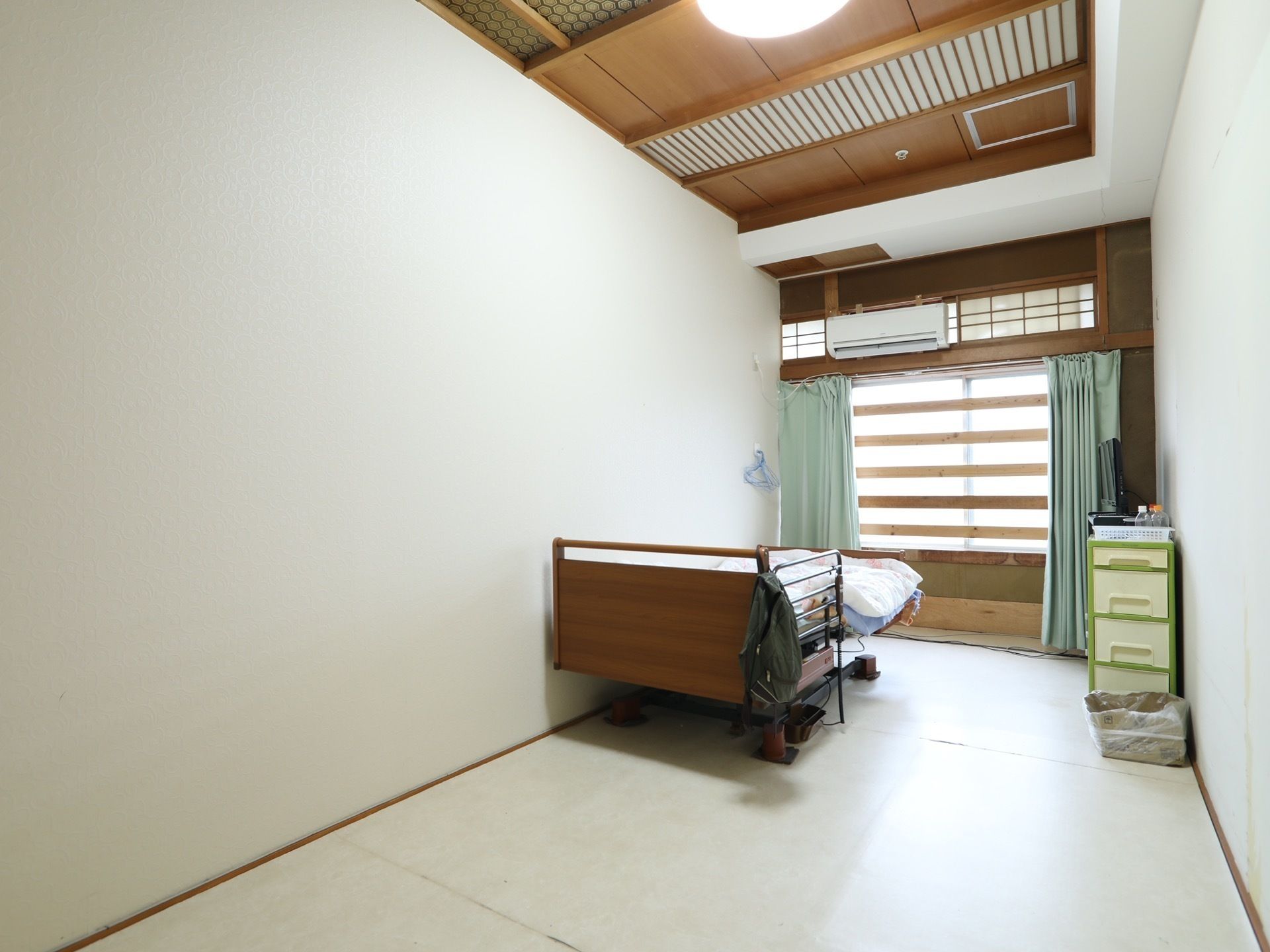 見通しの良い居室である。室内はシンプルな配置で、ベッドと収納ボックスがあり、エアコンが完備されている。