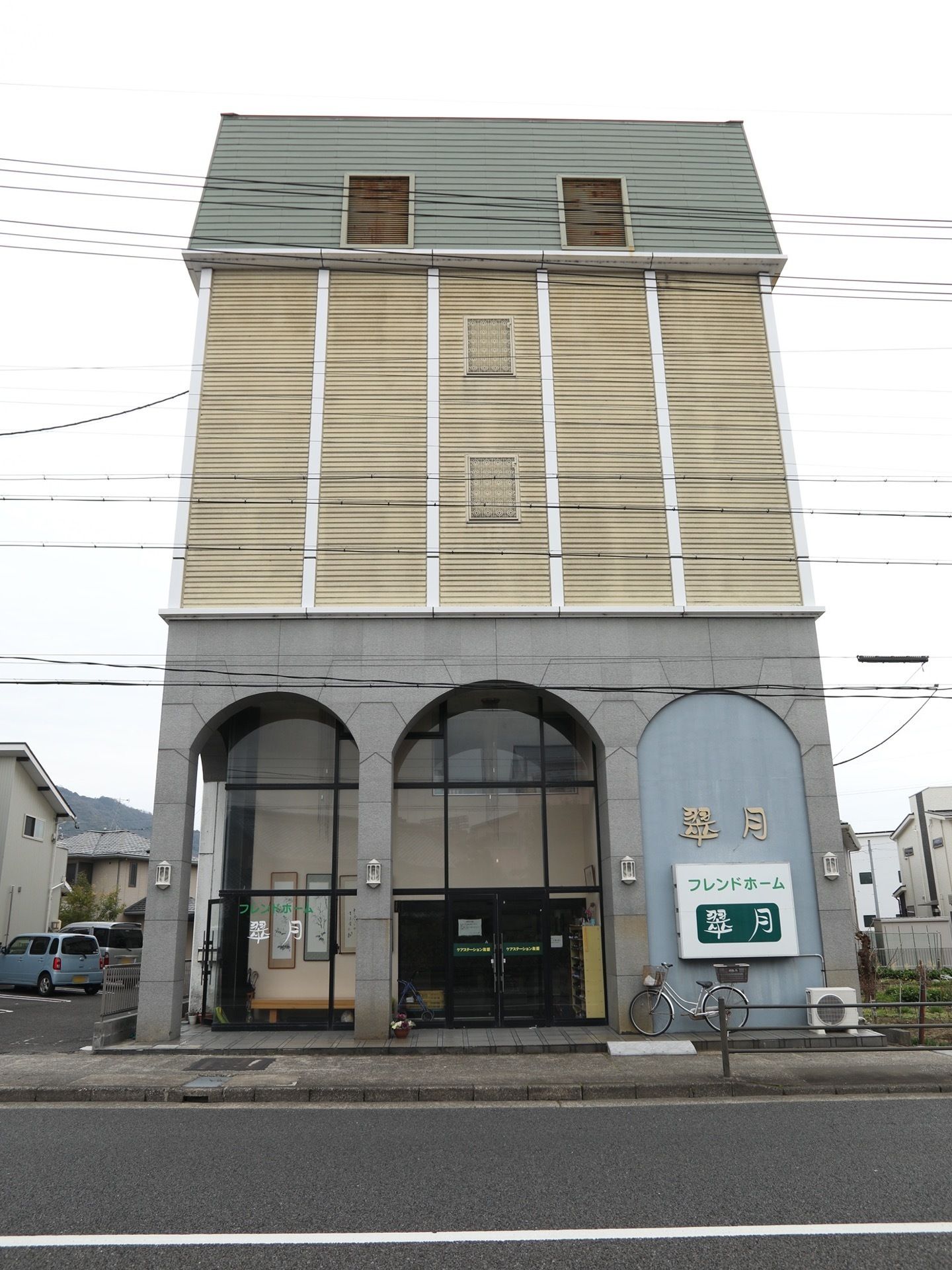 施設は、閑静な住宅地に位置している。施設の目の前を道路が走っていて、外壁には施設名が大きく記されている。