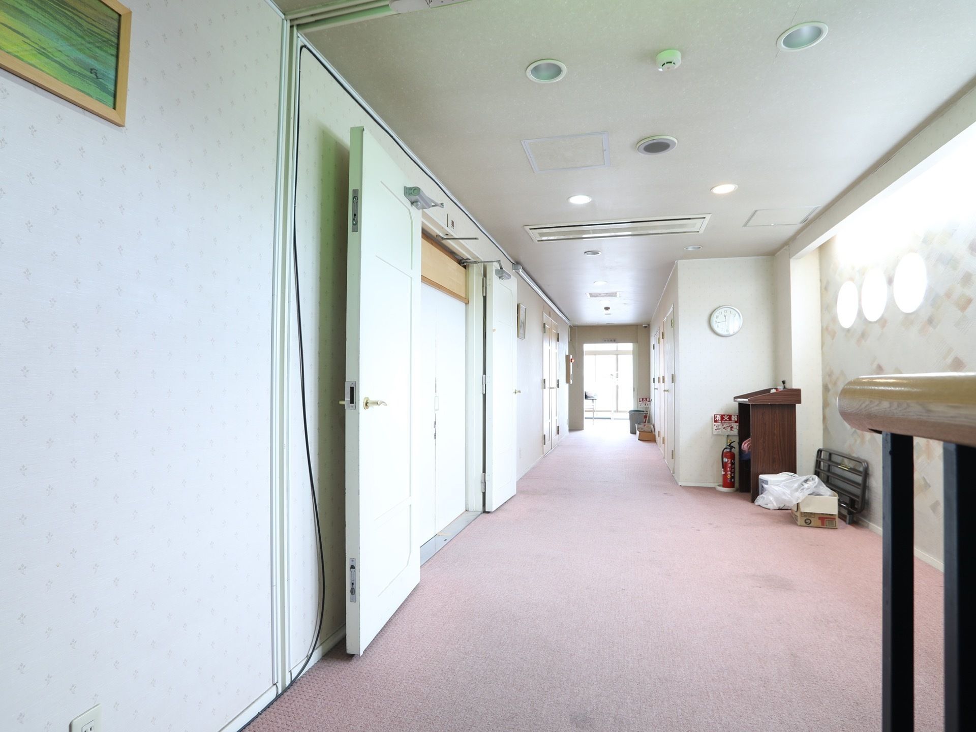 壁には丸く突き当りには大きな窓があり廊下内は明るくなっている。足元は絨毯が敷かれている。消火器も設置している。