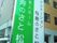白と緑の看板にはホーム名と併設事業所の名前が書かれている。奥にはブラウン系の建物が建っている。