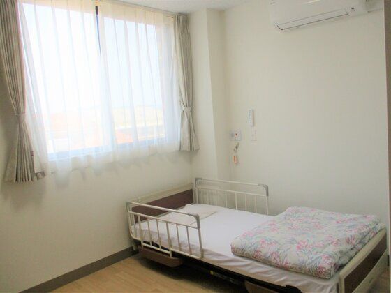 エアコンが付いたコンパクトな居室。寝具がセットされ、壁には緊急通報装置が付いている。