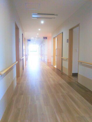 手すりが両サイドについた廊下。居室は木製の引き戸で、木のぬくもりが感じられる館内。