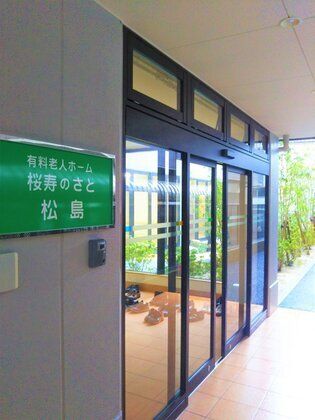 外壁にホーム名とインターフォンが設置されたエントランス。段差がなく、屋根も付いている。