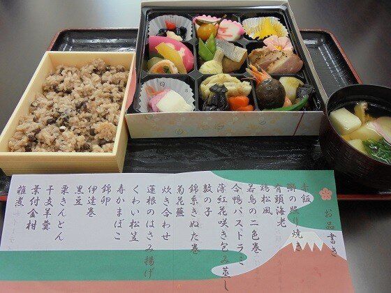 小さく区切られている弁当箱におせち料理が詰められ、炊き込みご飯と雑炊が、お品書きが添えられている。