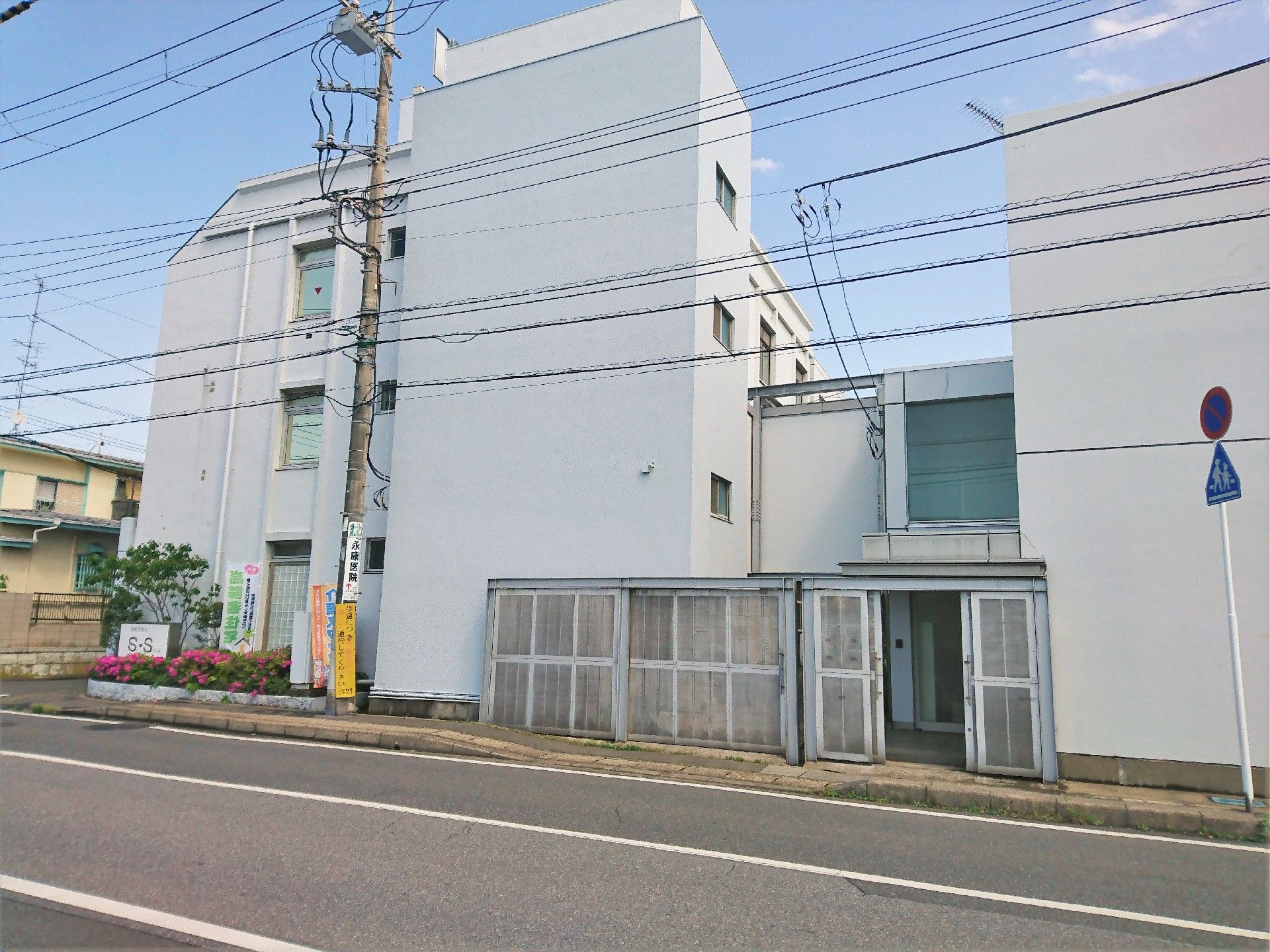 本館の建物の前には花壇や木が植えられたスペースがあり、ホームの看板も立っている。