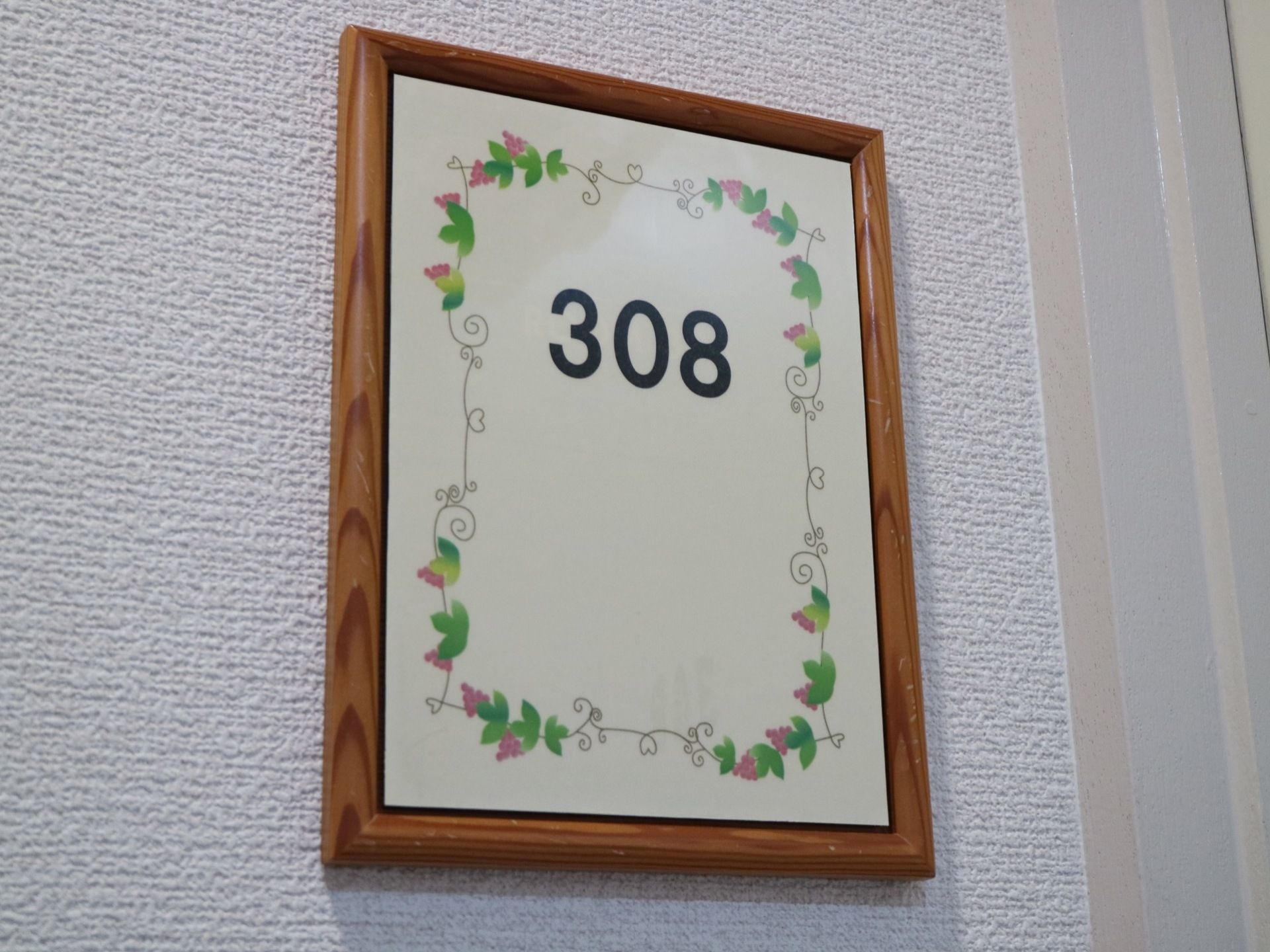 居室扉横の壁である。トールペイントと部屋番号が書かれたプレートが取り付けられている。木枠に設置されている。