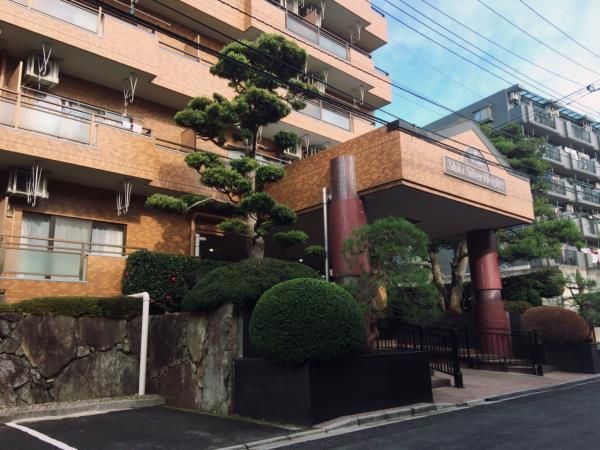 レンガ調の外壁が印象的な建物。玄関部分には屋根が付き、たくさんの木も植えられている。