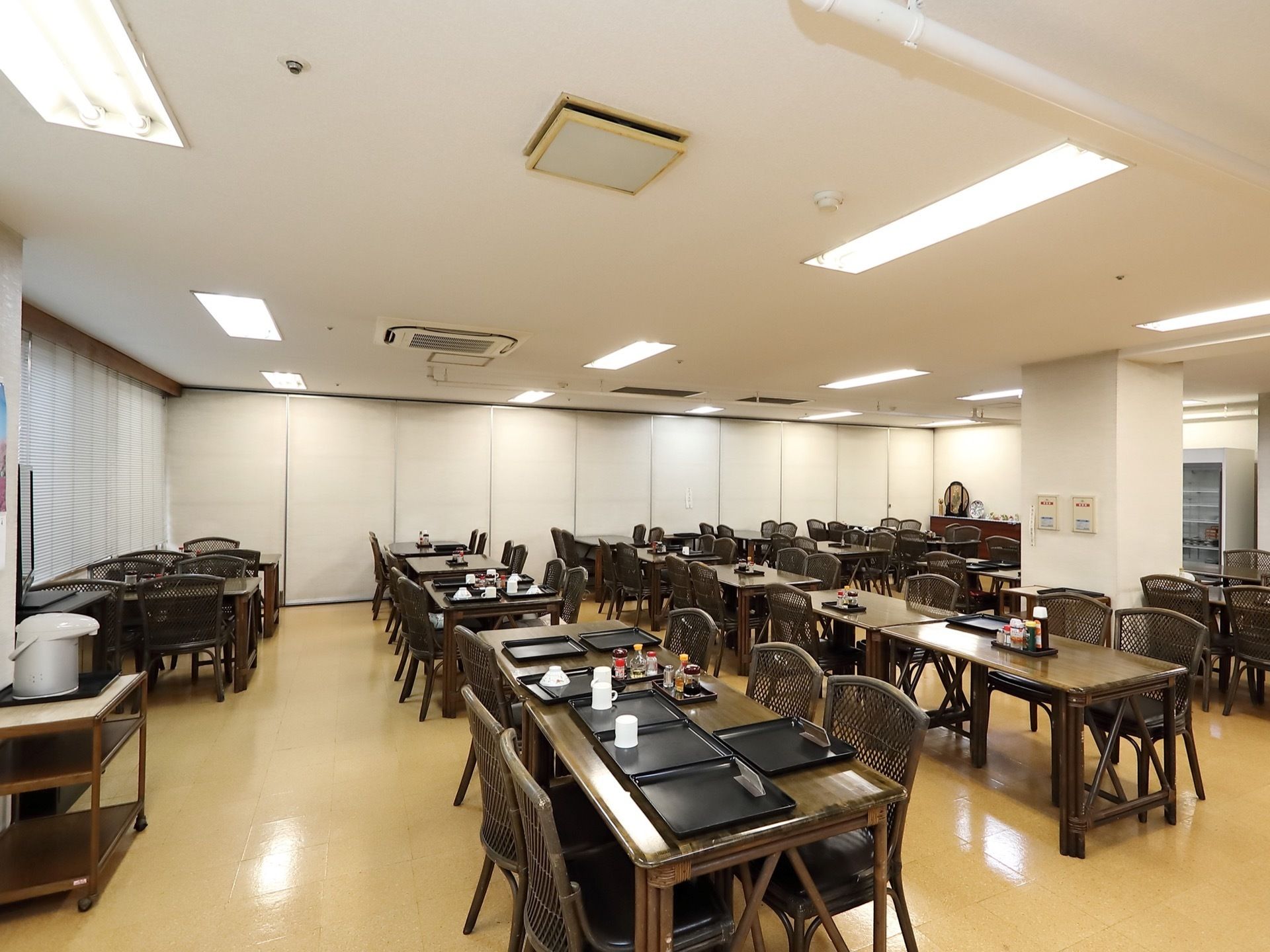 焦茶色のダイニングセットが整然と配置されている広間。手前のテーブルの上に複数のトレイが並べられている。