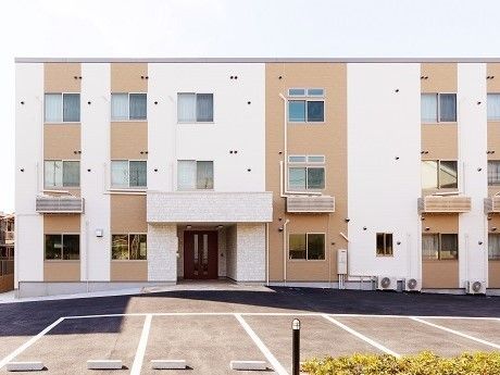 白とオレンジのツートンカラーの建物の写真。手前に広めの駐車場スペースがある