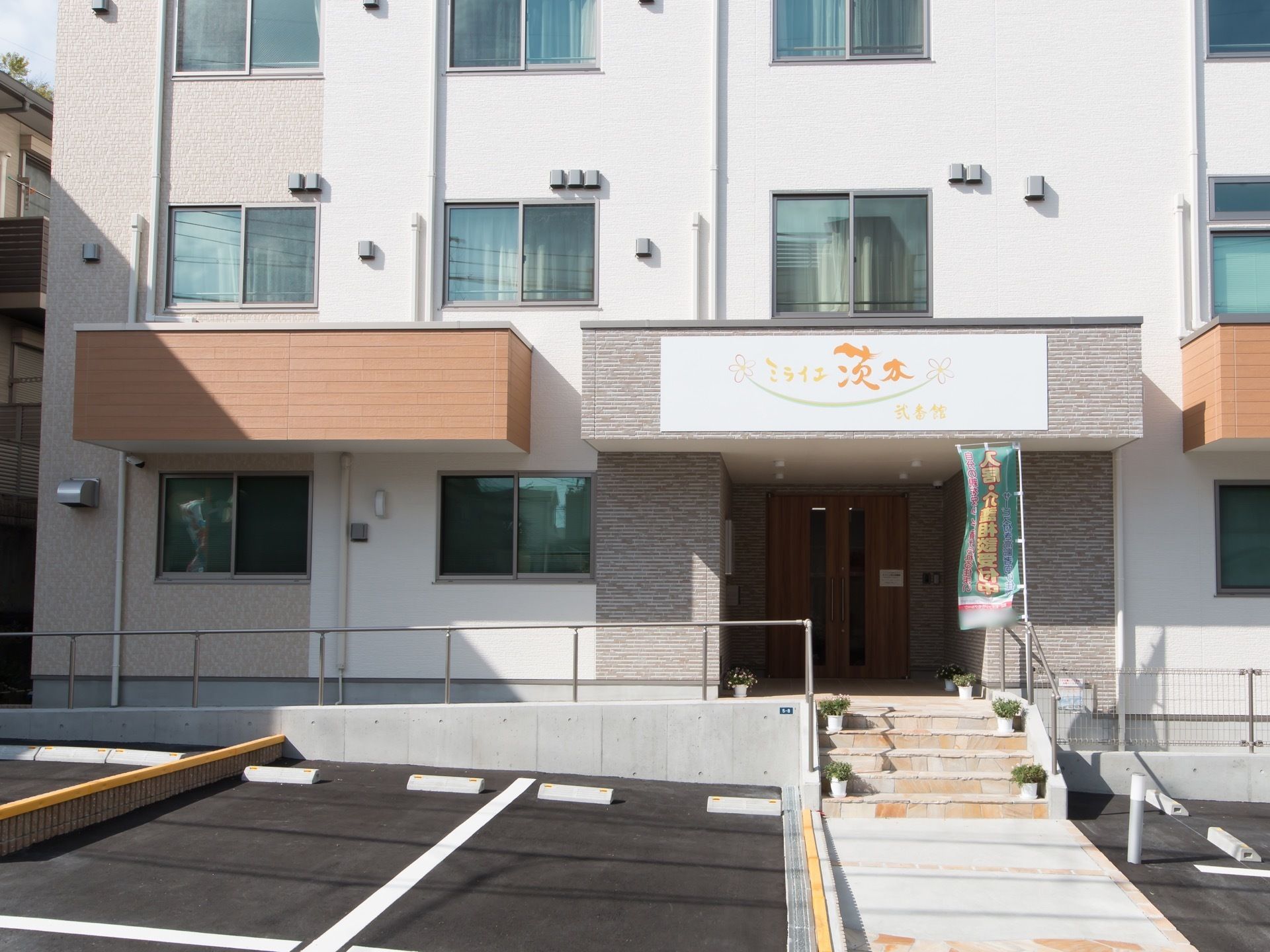 玄関の前には階段、壁に沿ってスロープがある。手すりもついて、安全に出入りすることができるような造りである。