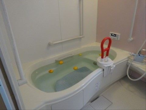 白いユニットバスにお湯が張られ入浴補助器具が設置された浴室