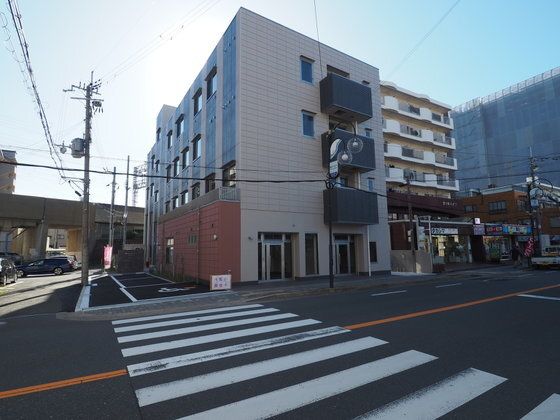 ４階建ての建物にはたくさんの窓が付き、周囲にはたくさんの建物もある。ベージュとグレーで落ち着いた雰囲気。