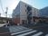 ４階建ての建物は落ち着いた色でまとめられ、出入り口が複数ある。周囲にはたくさんの建物もある。