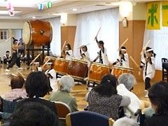 提灯が飾られた共有スペースで和太鼓の演奏を聴きいる入居者。