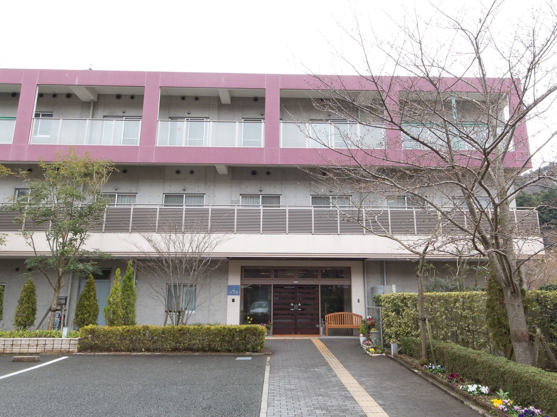 施設は、３階建てとなっている。玄関脇に木製の長椅子が設置されている。玄関までの垣根はきれいに整理され、下の花壇には草花が植栽されている。