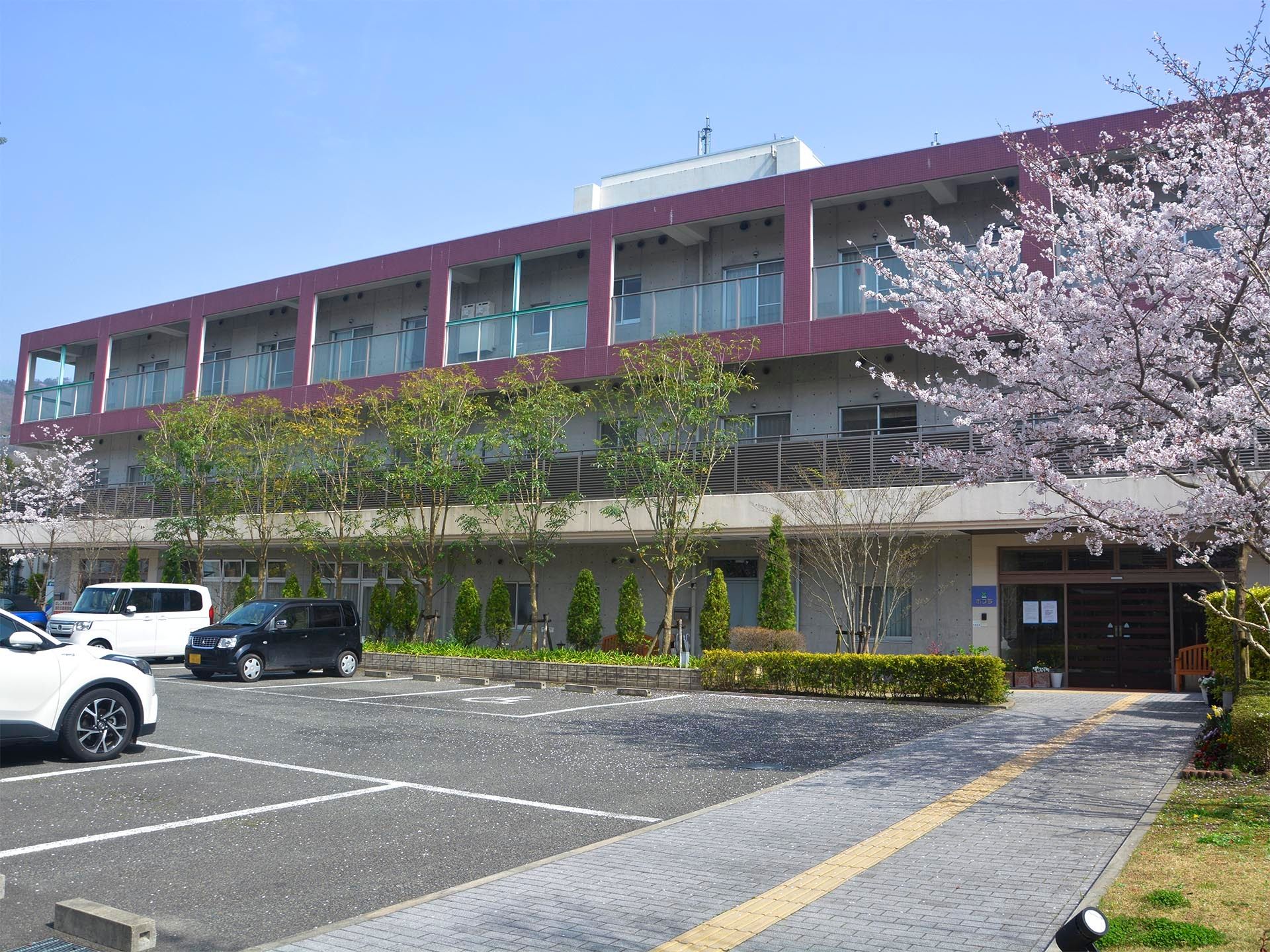 横に長い４階建ての建物。各フロアにベランダが付き、木もたくさん植えられている。