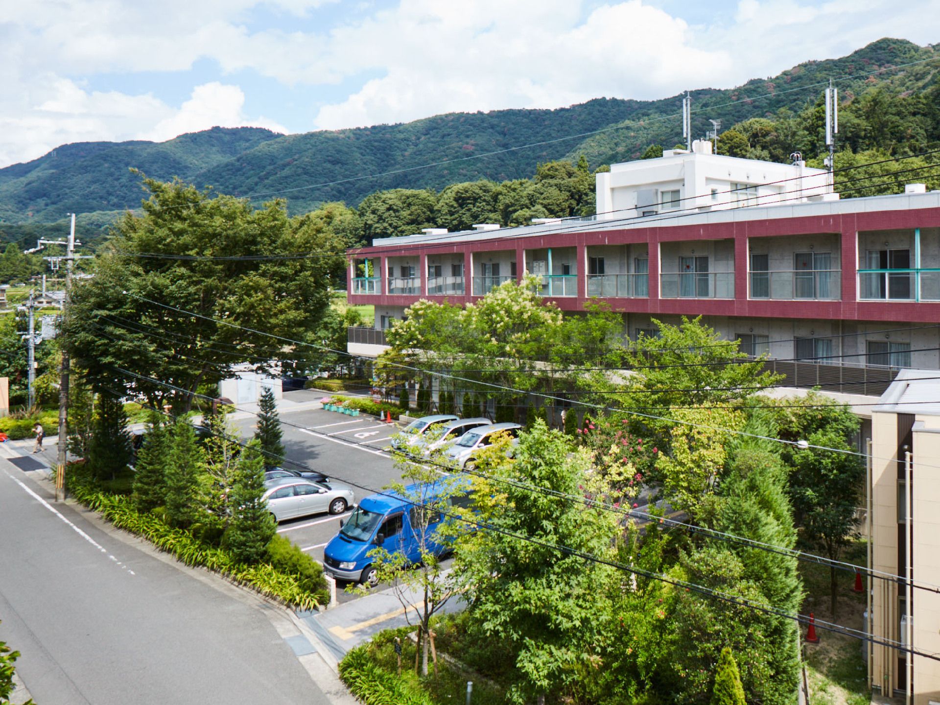 外壁はコンクリートの打ちっぱなしだが、３階部分はパープルに塗られている。建物の周りには、庭木が植栽されている。