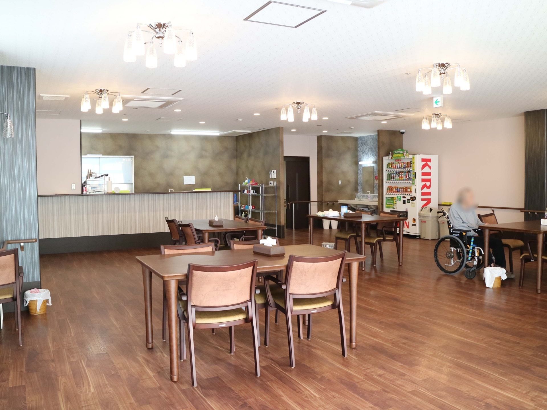 食堂には複数のテーブルと椅子が並べられている。テーブルの上にはテッシュボックスが置かれている。自動販売機もある。