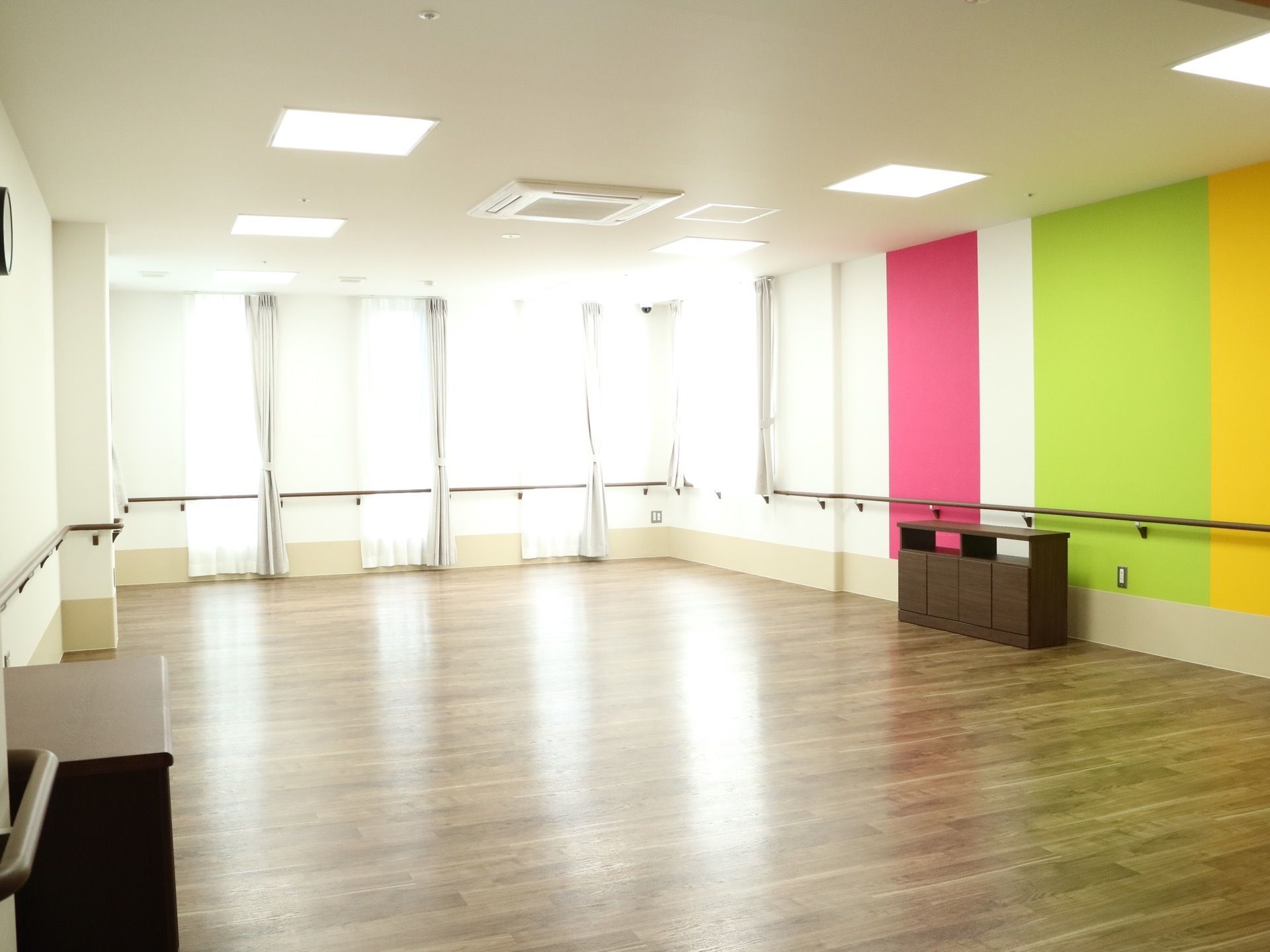 天井まで続く大きな窓のある広いホール。壁の一部が赤、黄緑、黄色とカラフルに塗られている。壁には手すりが設置されている。