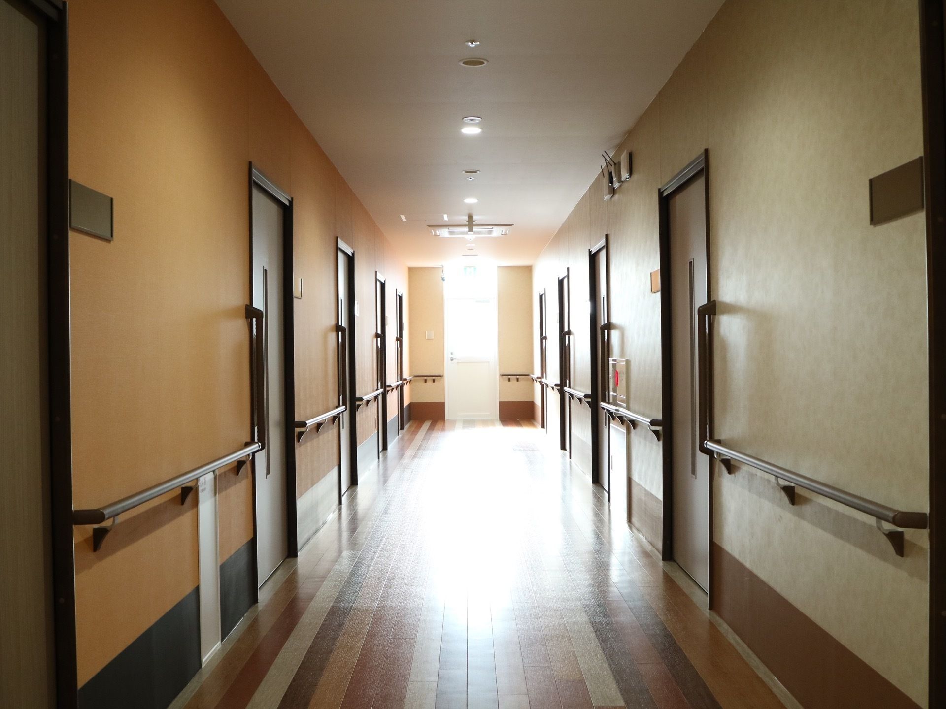 多色の寄せ木で作られたフローリングの床の廊下がある。両側には居室のドアが並んでおり、壁には手すりが設置されている。