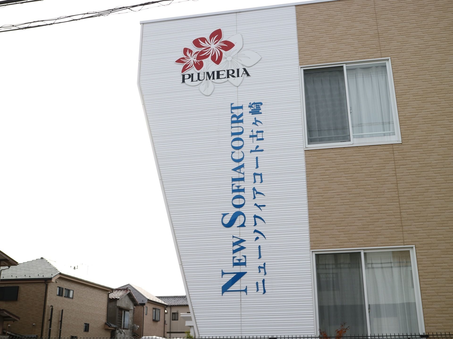 ベージュの壁の建物がある。壁の一部は白くなっており、青い文字で施設の名前とロゴが大きく書かれている。