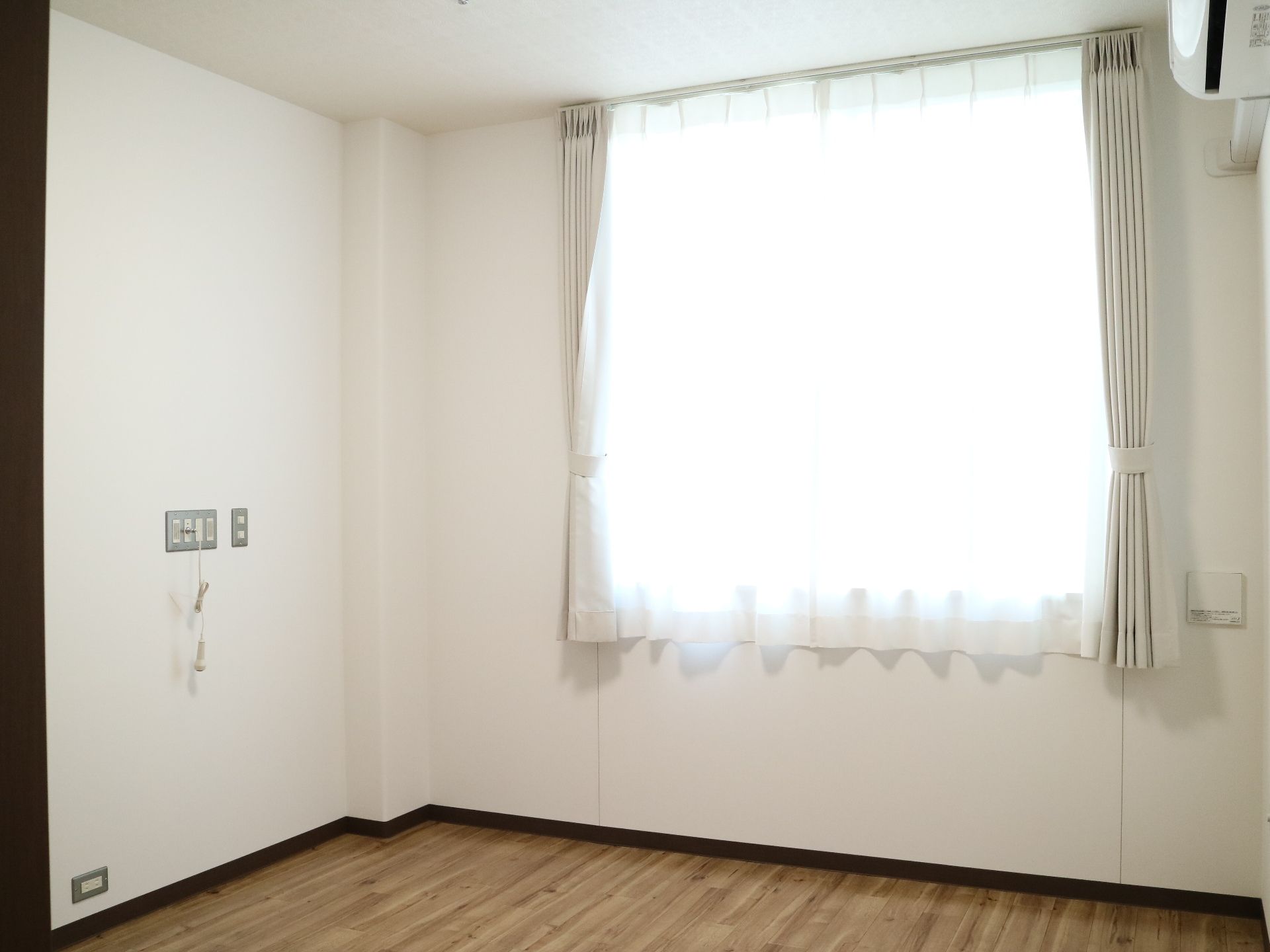 空調設備が揃い、レースのカーテンが掛かった窓がある居室