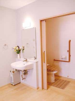 居室内に設置されているトイレと洗面台。家庭サイズで手すりが付いている