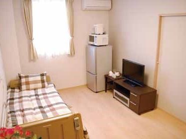 冷蔵庫や電子レンジ、テレビなどが置いてある小さな部屋の様子。窓やエアコンが付いているワンルーム