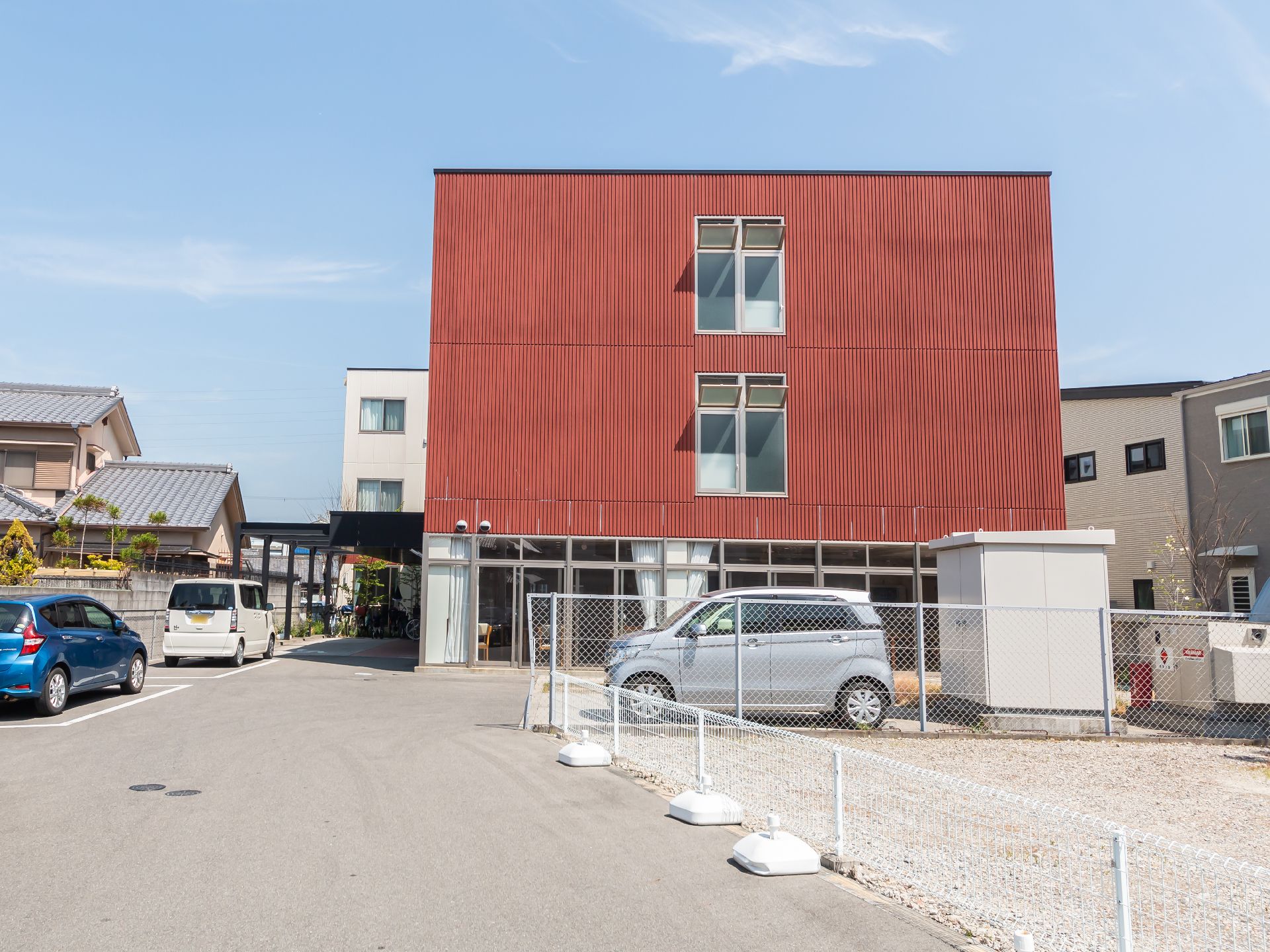 白とブラウンの３階建ての建物の玄関には屋根が付き、日当たりのいい場所に建っている。
