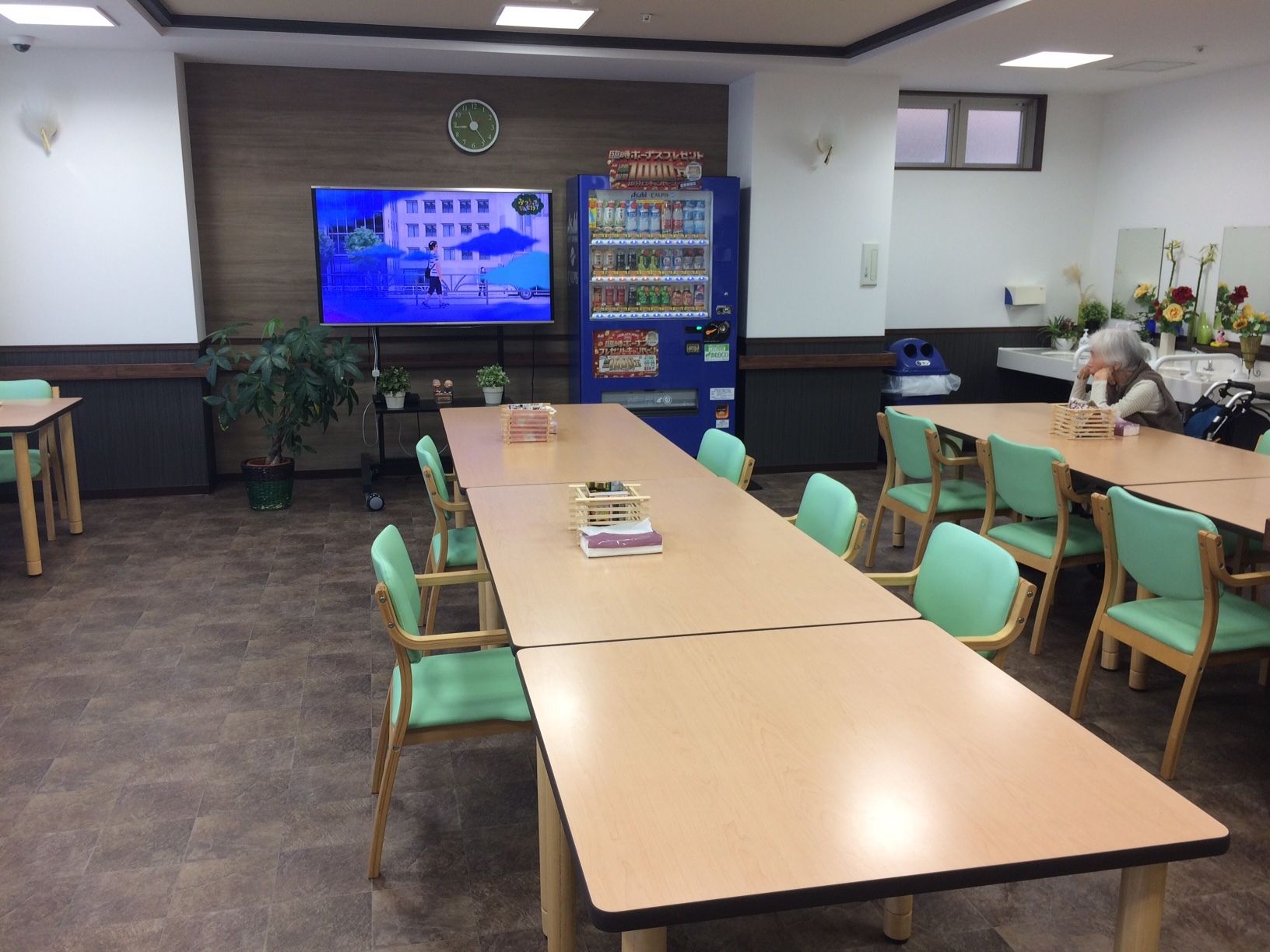 自動販売機やテレビが置かれた広い食堂には女性入居者が１名座っている。