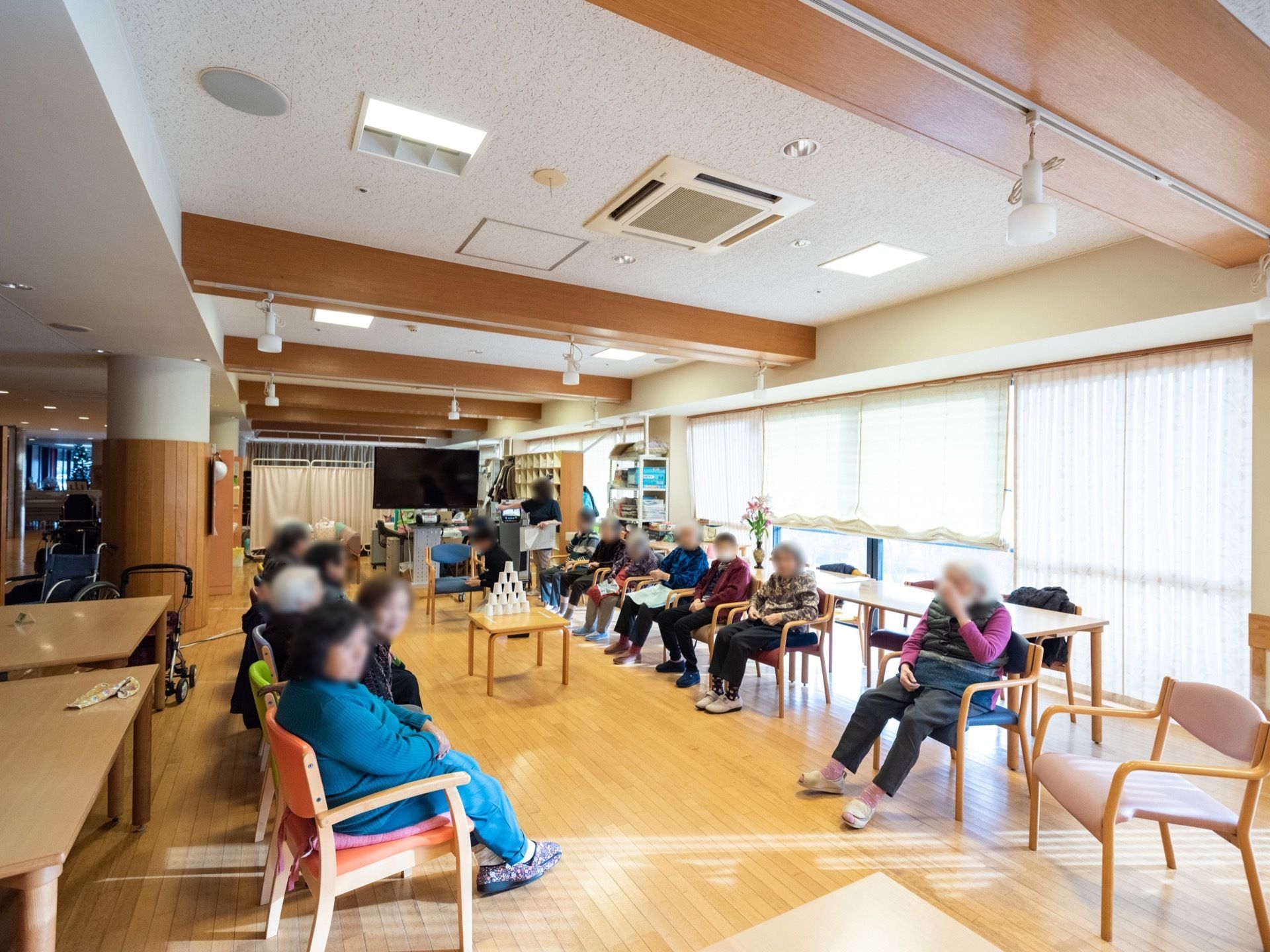 掃き出し窓が壁一面に備え付けられた、デイルームが設置されている。複数の入居者様が集い、レクリエーションを楽しんでいる。