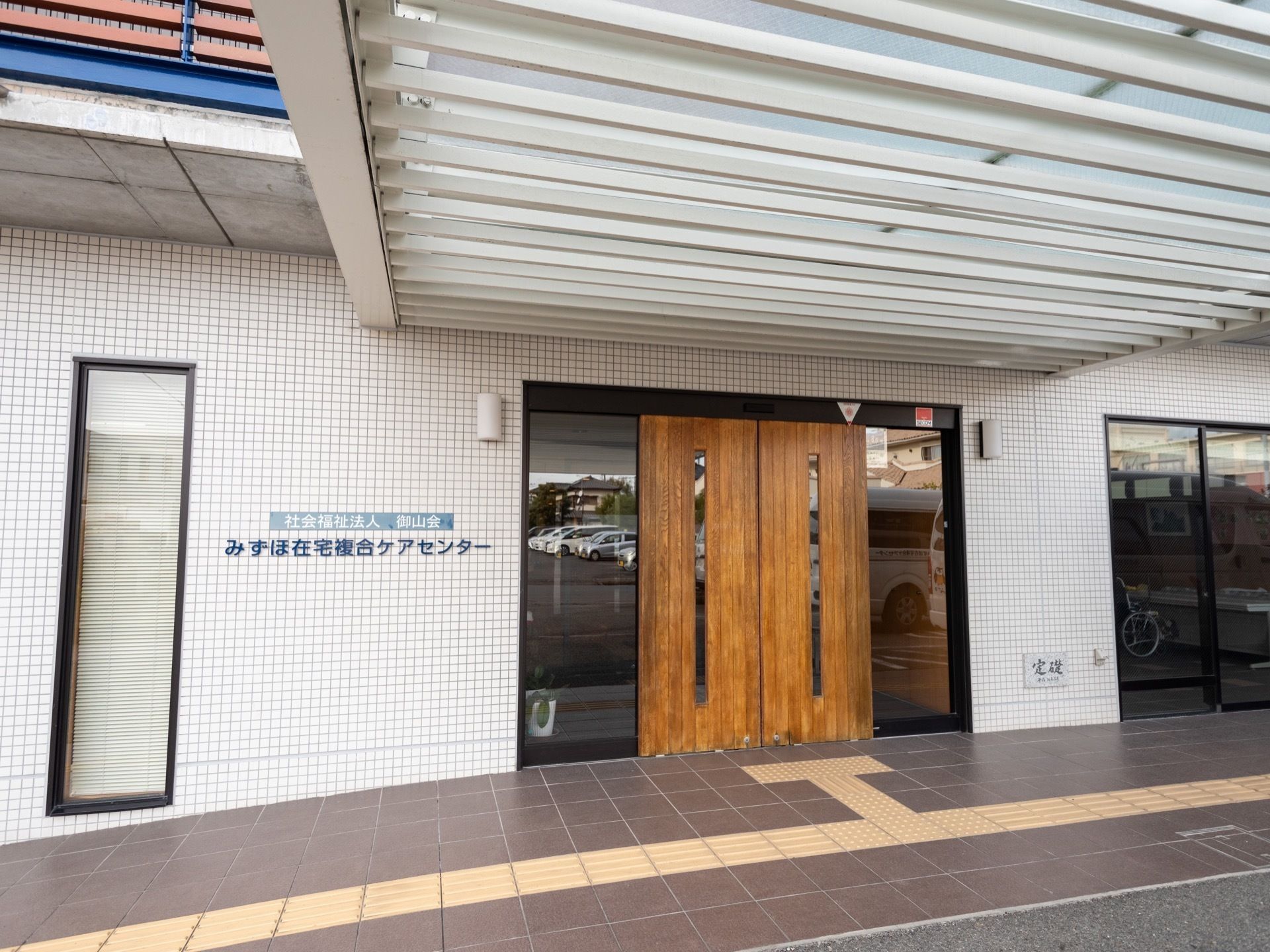 木材で造られた、玄関扉がある。館内へと続く通路には、黄色の点字ブロックが設置されている。