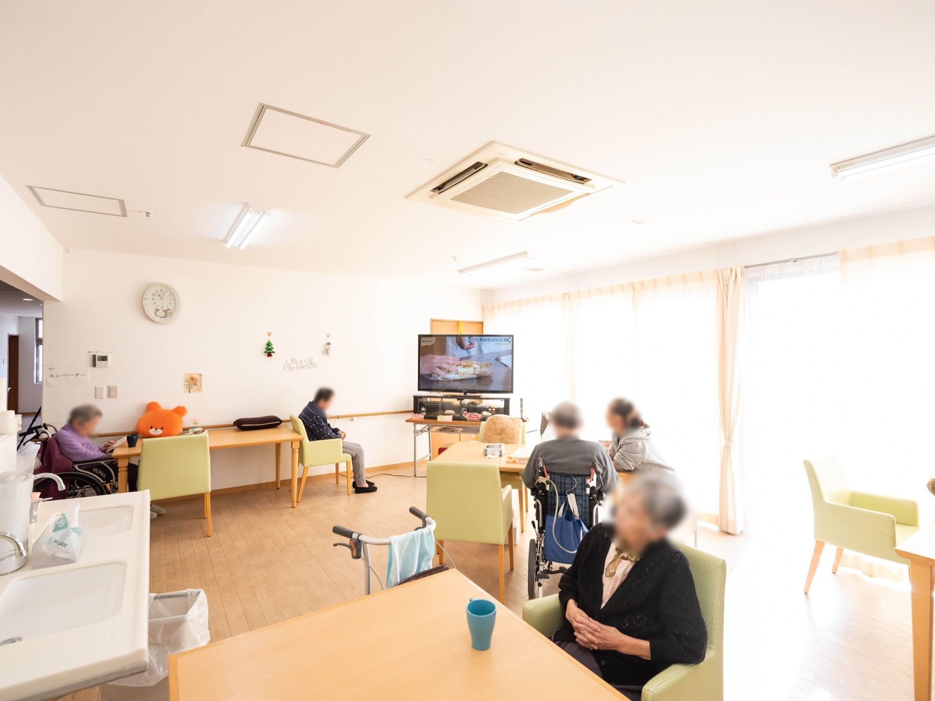 掃き出し窓が備え付けられた、明るい共有スペースである。コーナーにテレビが設置されている。手すりもある。