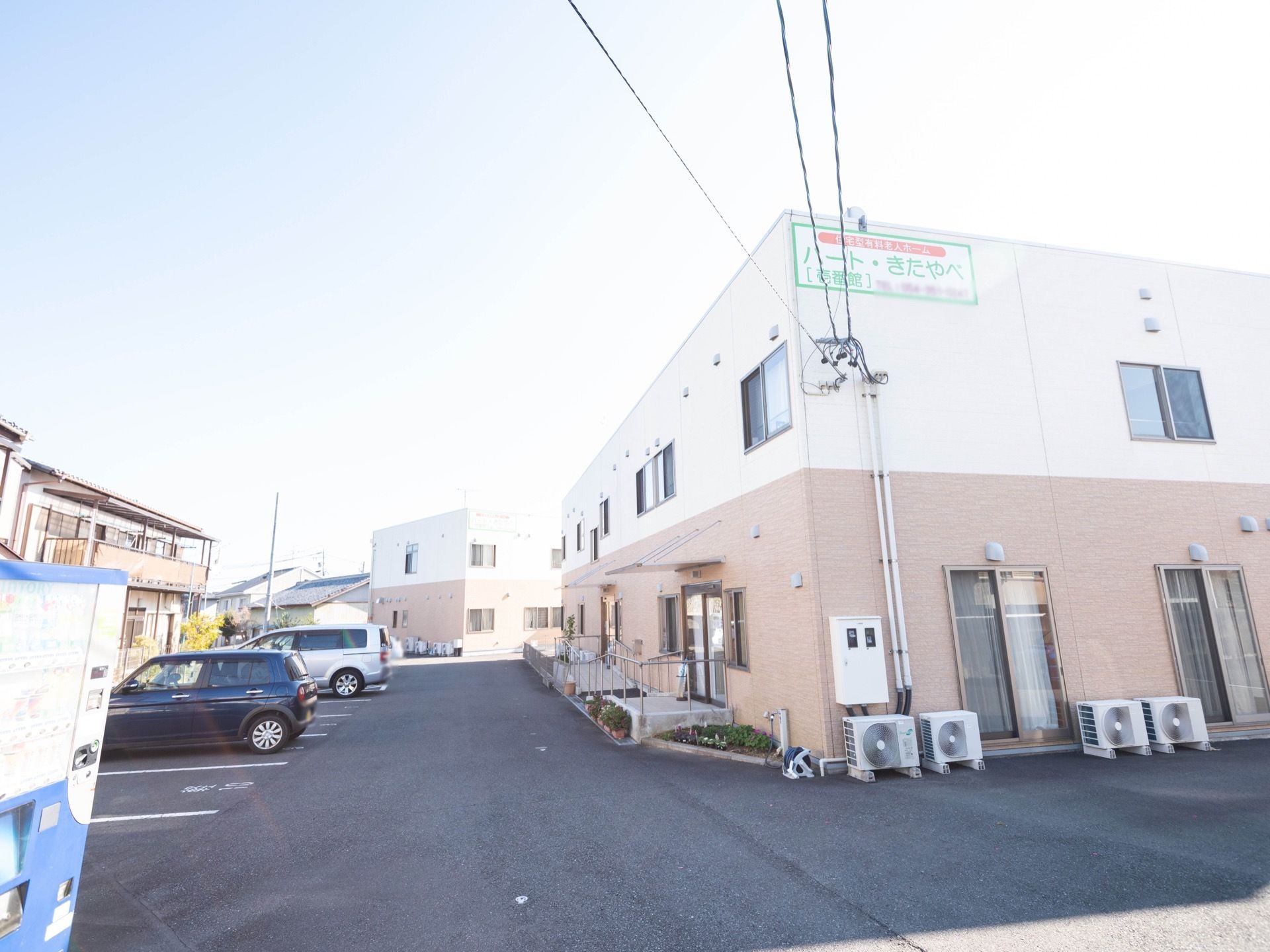 明るい色合いに施された、２階建ての施設である。外壁に看板が貼られている。白色の背景に、緑色の文字で施設名が書かれている。