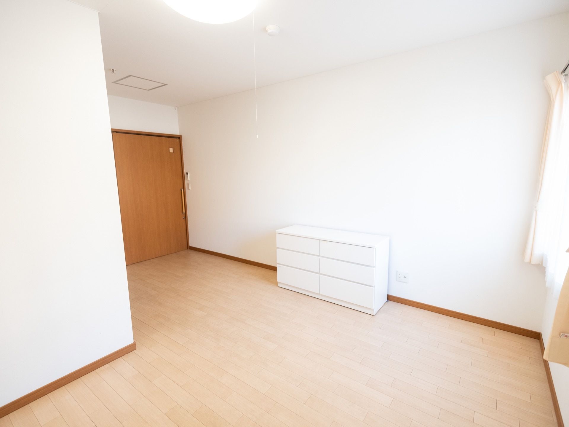 白色の３段チェストを居室に完備。天井に照明があり、明るく室内を照らしている。床色は明るめの茶系に、施工されている。