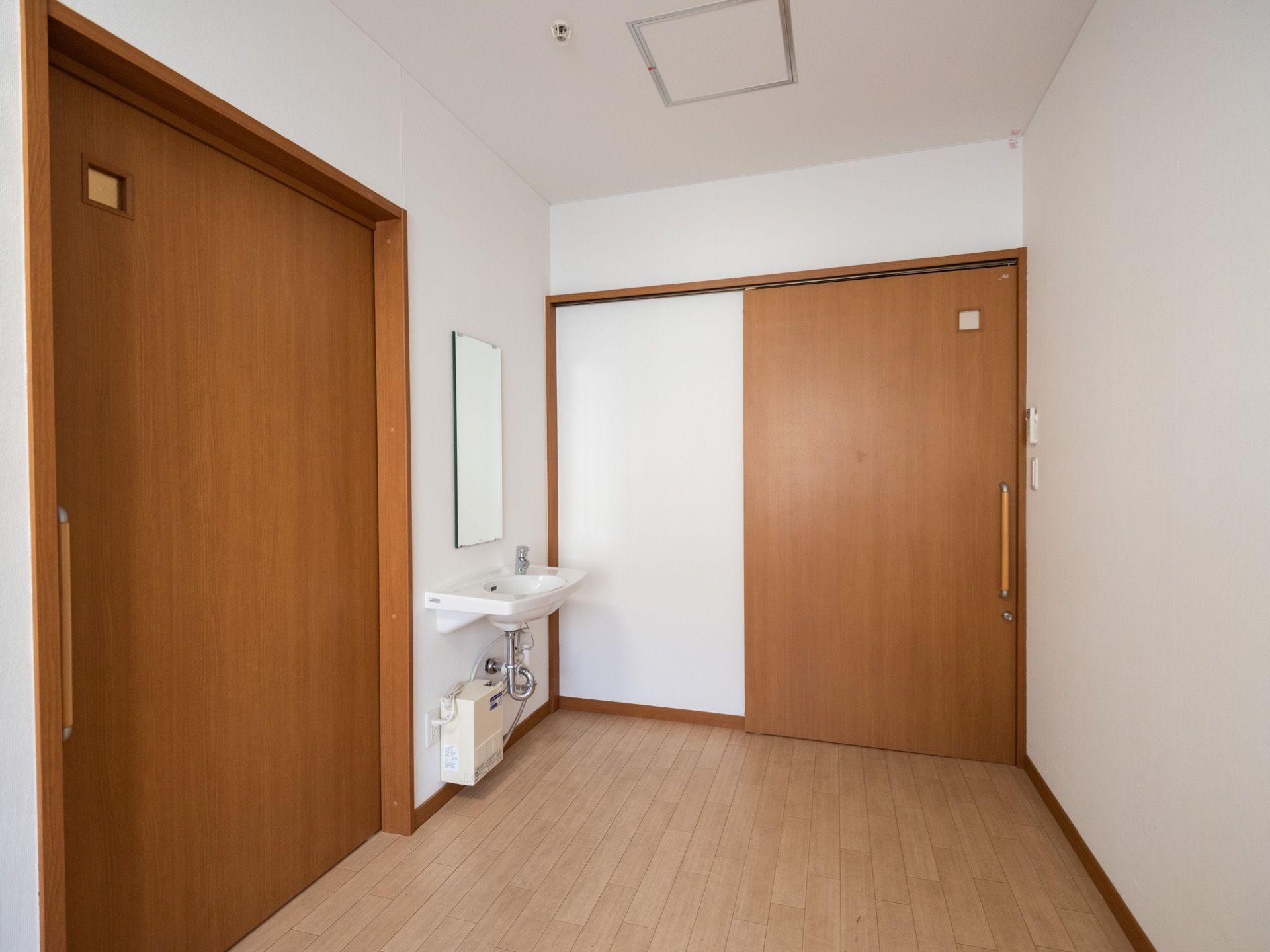 鏡付きの洗面台がある。居室の扉は引き戸式で、明かり窓も設置されてある。床はフローリング。