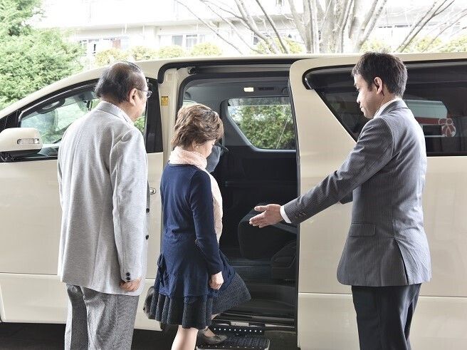 白い車の後部座席のドアを開けお客様を案内するスタッフ