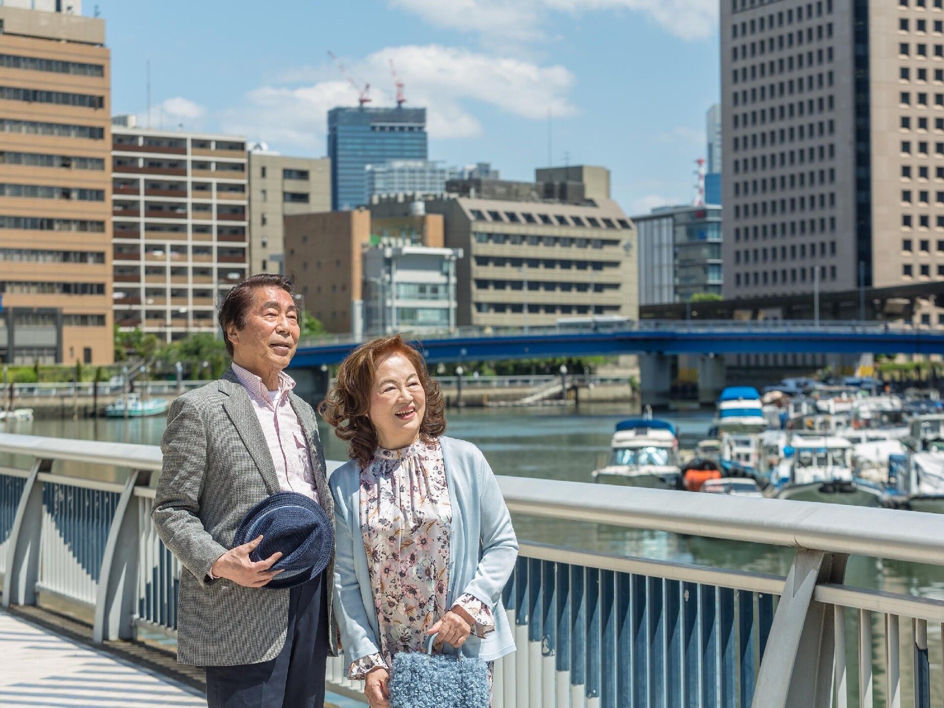 多くの船が止まっている川にかかる橋の上で並んでいるご夫婦