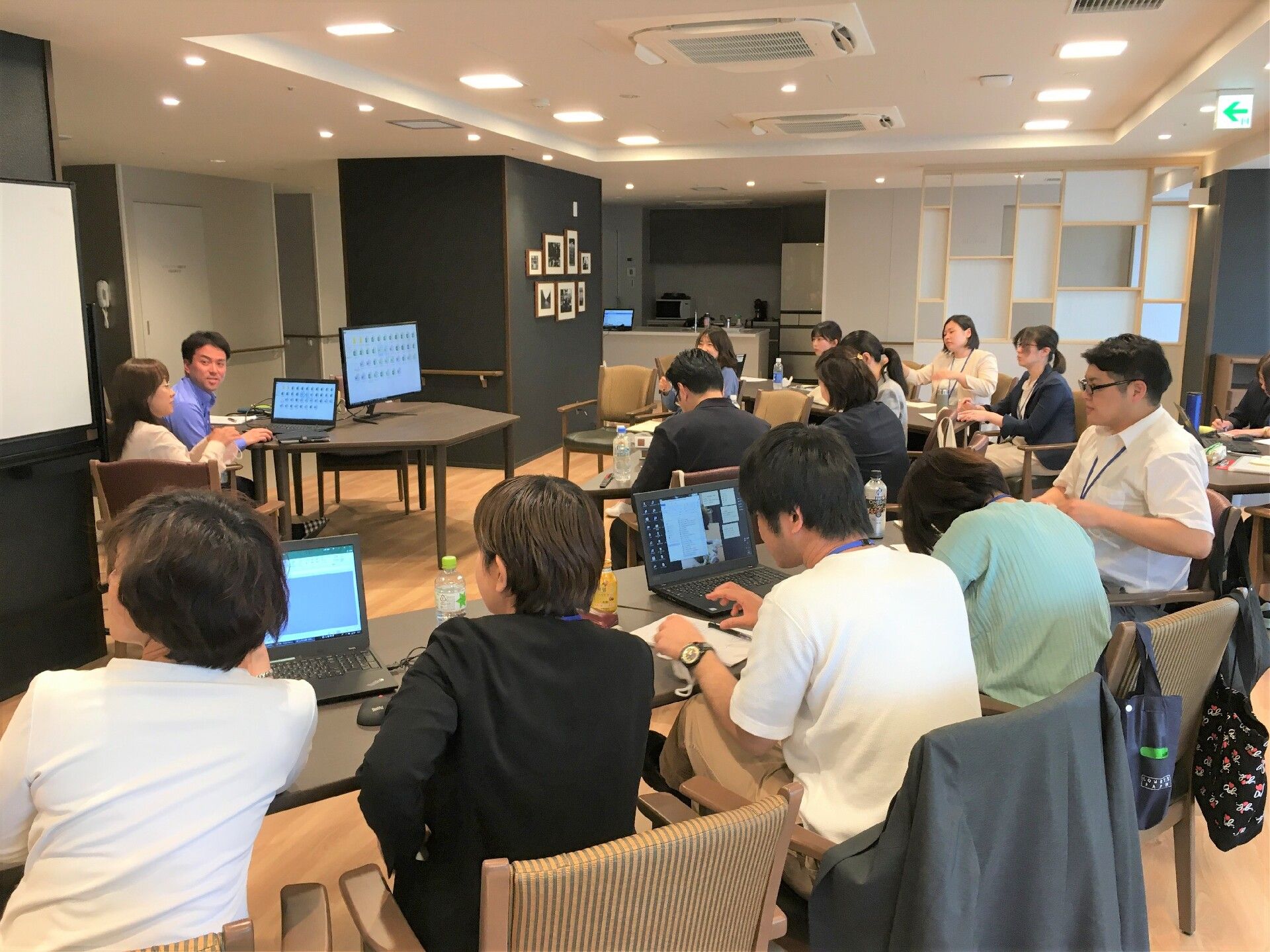 パソコンを各自持ち込んで勉強会を開いているスタッフたち。中央のテーブルに男女のスタッフ各1名がいて話している。
